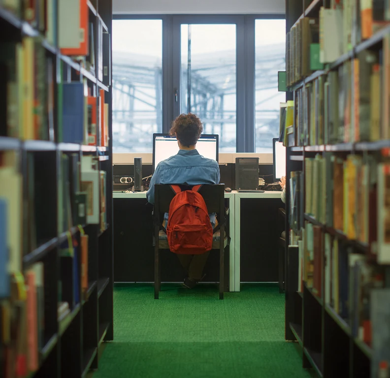 User searching the catalog on a computer between library shelves